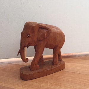 May include: A wooden elephant figurine with a light brown color. The elephant is standing on a base and has a long, thin tusk.