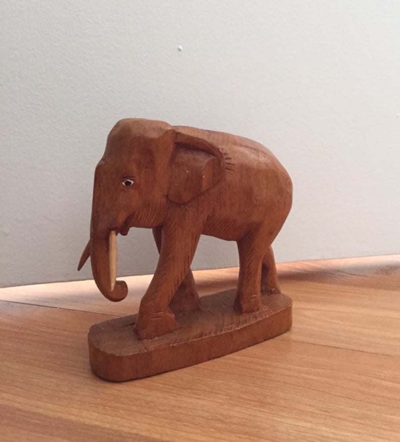 May include: A wooden elephant figurine with a light brown color. The elephant is standing on a base and has a long, thin tusk.