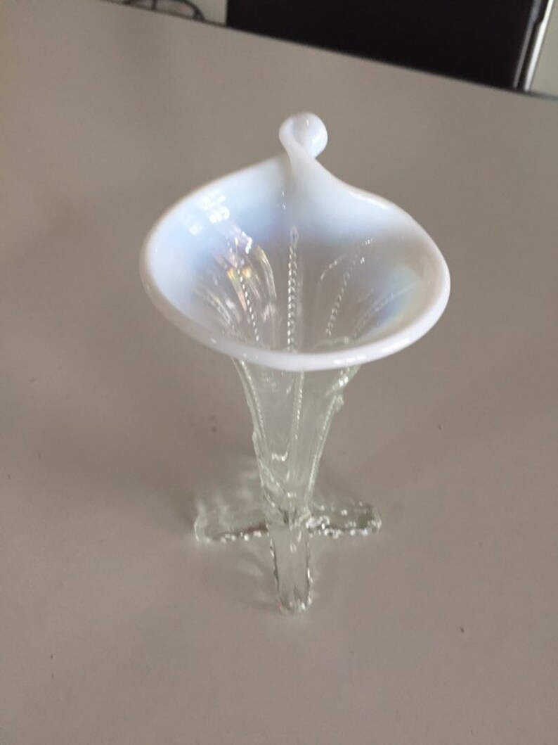 May include: A white iridescent glass vase with a flared top and a delicate, three-pronged base.