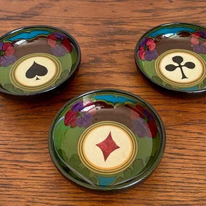 May include: Three small, round decorative bowls with playing card suit symbols. Each bowl features a different suit: spade, club, and diamond. The bowls have a dark brown interior, green and blue border, and floral accents.