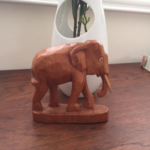May include: A hand-carved wooden elephant figurine with a brown finish. The elephant is standing on a small wooden base.