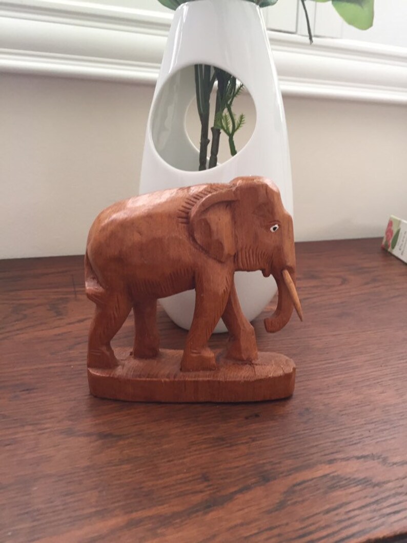 May include: A hand-carved wooden elephant figurine with a brown finish. The elephant is standing on a small wooden base.