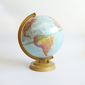 Może przedstawiać: Antyczna kula ziemska ze złotą podstawą. Kula jest niebieska z jasnoniebieskim oceanem i kolorowymi kontynentami. Kula jest przechylona, aby pokazać Amerykę Południową.