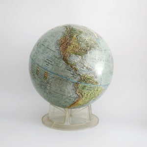 Może przedstawiać: Zabytkowy globus z kolorowymi kontynentami i jasnoniebieskimi oceanami, zamontowany na przezroczystym plastikowym stojaku. Globus zawiera szczegóły geograficzne i tekst, w tym słowo "EXPLORE" i liczby "1825-805-528".