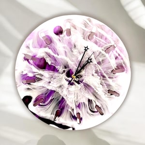 May include: Round wall clock with a white background and a purple and white abstract floral design. The clock has black hands and star-shaped markers at the 12, 3, 6, and 9 o'clock positions.