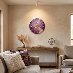 A circular wall clock featuring a deep purple resin base with a central, textured band of gold-toned metallic flakes and crystals. The clock face includes simple, thin gold-colored hour markers and matching central hands for timekeeping.