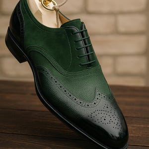 May include: A green and black leather dress shoe with a wingtip design. The shoe features a textured toe cap and a smooth, glossy finish on the toe. The shoe is on a wooden shoe form.