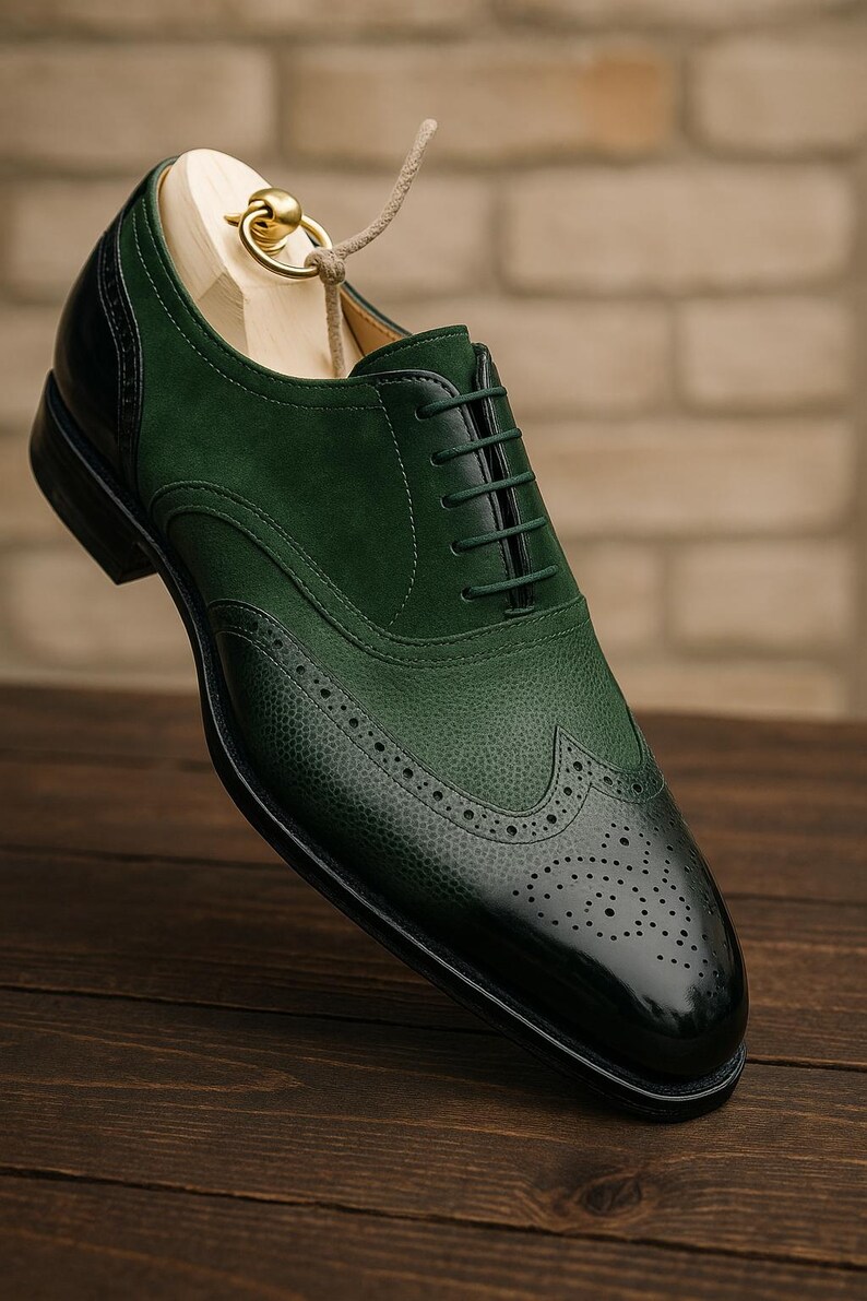 May include: A green and black leather dress shoe with a wingtip design. The shoe features a textured toe cap and a smooth, glossy finish on the toe. The shoe is on a wooden shoe form.
