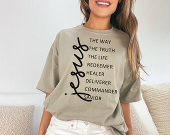 May include: A light green oversized t-shirt with the word "Jesus" written vertically in black. The text is followed by a list of words describing Jesus: "The Way, The Truth, The Life, Redeemer, Healer, Deliverer, Commander, Savior". The t-shirt is on a model wearing white denim shorts. The text "Size XL" is visible in the bottom right corner of the image.
