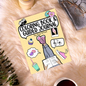May include: A yellow colouring book and guided journal cover with a cartoon illustration of a person reading a book with their legs in the air. The cover also features a camera, ice cream cone, cupcakes, macarons, music notes, and bubble tea.