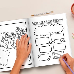 May include: A black and white colouring book page with a drawing of a camera and flowers. The page is open to a spread that includes the text "Things that make me feel loved:" and several blank shapes for writing.