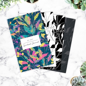 May include: A set of three 90-day spiritual journals with different floral designs. The journals have a dark blue, black and white, and gray cover with a floral pattern.