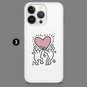 May include: White phone case featuring a pink heart design held up by two stick figures in black. The heart has radiating lines, and the case has a glossy finish. The phone case is designed for a smartphone.