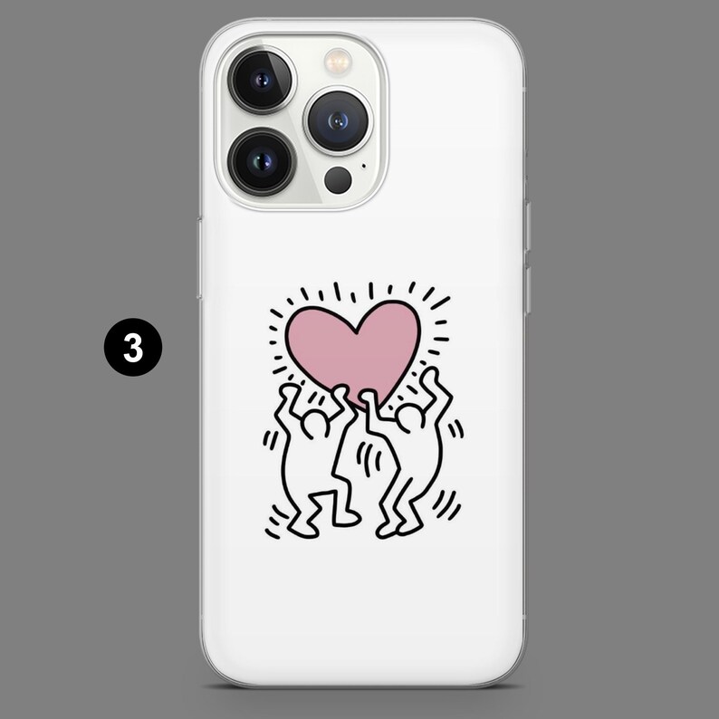 May include: White phone case featuring a pink heart design held up by two stick figures in black. The heart has radiating lines, and the case has a glossy finish. The phone case is designed for a smartphone.