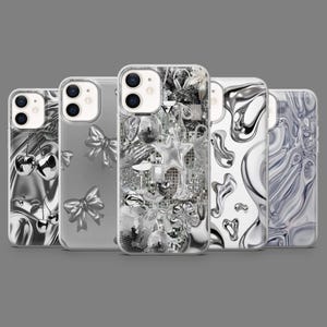 May include: A collection of five phone cases with various designs. The cases feature silver-toned embellishments, including cherries, bows, disco balls, stars, and abstract patterns. The cases are displayed against a gray background.