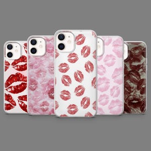 May include: A collection of five phone cases with various lip print designs. The cases feature different shades of red and pink lip imprints on white and pink backgrounds. The cases are arranged in a row against a gray backdrop.