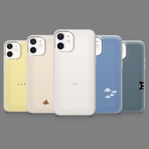 Puede incluir: Una colección de cinco fundas para teléfono de varios colores. Las fundas presentan diseños minimalistas, incluyendo una funda amarilla con una cara de pato, una funda beige con un oso, una funda blanca con una carita sonriente, una funda azul con nubes y una funda gris con un gato.