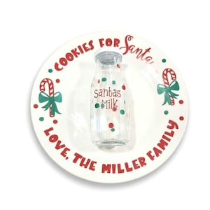May include: A white ceramic plate featuring red text reading Cookies for Santa and Love, The Miller Family, with green and red candy cane graphics. A clear glass milk bottle with a silver lid sits in the center, labeled Santas Milk in red text.
