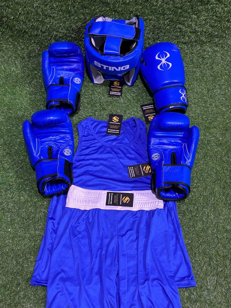 May include: A complete blue boxing set, including a head guard with "STING" text, boxing gloves, a tank top, and shorts. The set is arranged on a green surface. The gloves have a white infinity symbol.