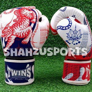 Puede incluir: Un par de guantes de boxeo blancos con gr&aacute;ficos en rojo y azul. El guante izquierdo muestra una ilustraci&oacute;n de un tigre rojo y el texto SHAHZUSPORTS. El guante derecho presenta un dise&ntilde;o de loto azul. Ambos tienen el logo TWINS SPECIAL.