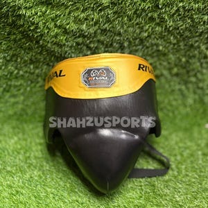 Puede incluir: Protector atl&eacute;tico negro y amarillo con el texto "RIVAL" en la banda amarilla. La copa tiene una carcasa protectora negra y una banda amarilla con el logotipo de la marca. El texto "Shahzusports" est&aacute; impreso en la copa.
