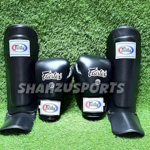 Op de afbeelding: Zwarte bokshandschoenen en scheenbeschermers met het "Fairtex" logo op een groene ondergrond. De tekst "SHARZUSPORTS" is op de afbeelding gedrukt.