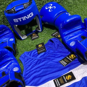 May include: A collection of blue boxing equipment, including gloves, a head guard with "STING" printed on it, a tank top, and shorts. The gloves and headgear have white logos. The tank top and shorts are blue with white accents.