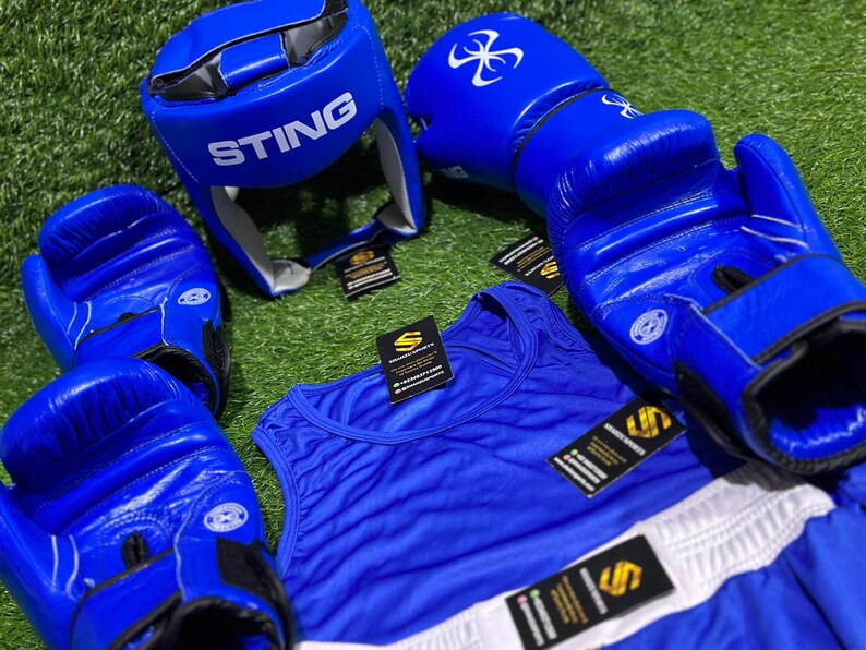 May include: A collection of blue boxing equipment, including gloves, a head guard with "STING" printed on it, a tank top, and shorts. The gloves and headgear have white logos. The tank top and shorts are blue with white accents.