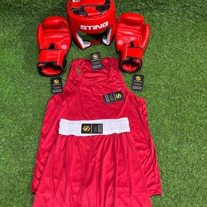 May include: A complete red boxing set, including gloves, headgear with "STING" text, a tank top, and shorts with a white waistband. The set is arranged on a green surface, ideal for boxing enthusiasts.