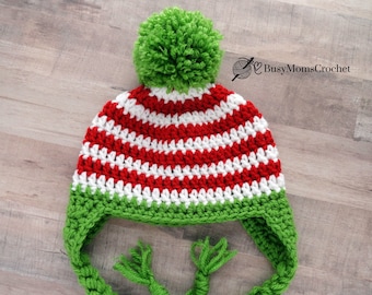 May include: A red and white striped crochet hat with a green pom pom and green ear flaps. The hat has a long green crocheted tie.