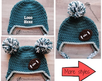 May include: Three crocheted hats in teal green with white pom poms. One hat has a brown football applique, one has a white embroidered logo, and one has ear flaps. The hats are on a wood background.