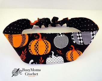 May include: A black headband with an orange pumpkin pattern, white polka dots, and a gray and white diamond pattern. The headband has an elastic band and is likely for Halloween or fall.