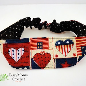 May include: A red, white, and blue patterned headband with a black elastic band. The pattern features hearts, stars, and American flags. The headband is made of fabric and has a polka dot lining.