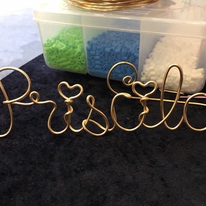 May include: Gold wire sculpture of the name "Priscilla" with two hearts incorporated into the design.