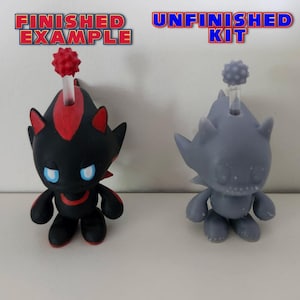 May include: A finished and unfinished 3D printed model of a black and red character with a spiky head. The finished model is painted black and red, while the unfinished model is grey. The text "FINISHED EXAMPLE" is above the finished model, and the text "UNFINISHED KIT" is above the unfinished model.