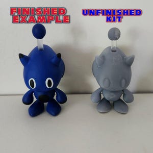 May include: A blue and grey plastic toy robot figurine. The blue figurine is labelled "Finished Example" and the grey figurine is labelled "Unfinished Kit".