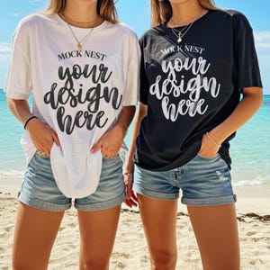 Pode incluir: Duas camisetas, uma branca e outra preta, cada uma com o texto "MOCK NEST your design here" em estilo manuscrito. As camisetas são combinadas com shorts jeans. O fundo mostra uma praia com água e céu azuis.