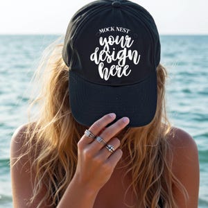 May include: Black baseball cap with the text "MOCK NEST your design here" in white script. The cap is worn by a person with long blonde hair, with the ocean in the background.