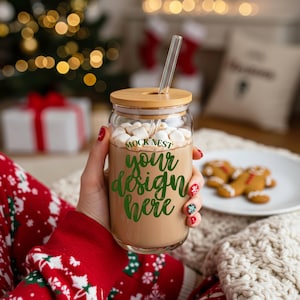 May include: A clear glass tumbler with a bamboo lid and a clear straw, filled with a hot chocolate drink and marshmallows. The tumbler has the text "MOCK NEST your design here" in green. The person is wearing a red Christmas sweater.