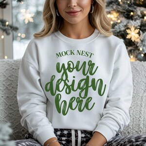 Puede incluir: Sudadera blanca de cuello redondo con el texto "MOCK NEST your design here" en verde. La sudadera es lisa y sencilla, perfecta para mostrar un diseño personalizado. La modelo lleva pantalones con estampado en blanco y negro.