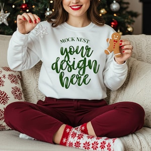Może przedstawiać: Biała bluza z napisem "MOCK NEST your design here" w zielonym kolorze. Osoba trzyma ozdobę w kształcie płatka śniegu i piernikowego ludzika. Osoba ma na sobie bordowe spodnie i czerwono-białe skarpetki w płatki śniegu.