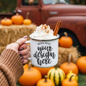 Könnte beinhalten: Weißer Emaillebecher mit dem Text "MOCK NEST your design here", gefüllt mit Schlagsahne, Zimt und einem Zimtstange. Der Becher wird vor Kürbissen und einem roten Oldtimer-Truck gehalten, was ein Herbstthema hervorruft.