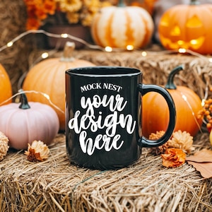 Pode incluir: Uma caneca de café preta com o texto "MOCK NEST your design here" em escrita branca. A caneca é cercada por abóboras, cabaças e folhagens de outono, criando um tema sazonal de outono.