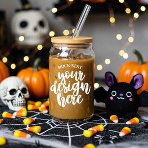 May include: A clear glass tumbler with a bamboo lid and a glass straw, filled with a brown beverage. The text "MOCK NEST your design here" is on the front. Halloween-themed with pumpkins, candy corn, a skull, and a plush bat.