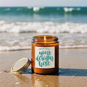 May include: A lit candle in a brown glass jar with a gold lid, sitting on a sandy beach with ocean waves in the background. The candle has a white label with the text "MOCK NEST your design here" in teal script.