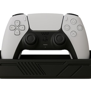 以下が含まれることがあります： 黒い充電スタンドに置かれた、白と黒のPlayStation 5コントローラー。 コントローラーは、ボタンとジョイスティックを備えた対称的なデザインです。 スタンドは幾何学模様です。