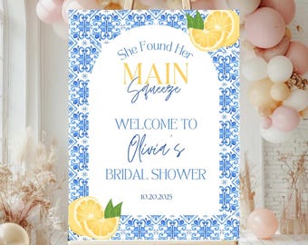 May include: A bridal shower welcome sign with a blue and white tile design border. The sign reads "She Found Her Main Squeeze, Welcome to Olivia's Bridal Shower" with lemon illustrations. The date 10.20.2025 is also displayed.