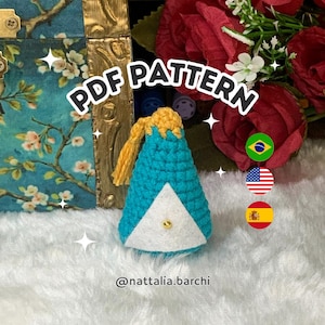 May include: A crocheted teal and white ornament with a gold tassel and a gold bead. The text "PDF PATTERN" is displayed above the ornament. The ornament is on a fluffy white surface.