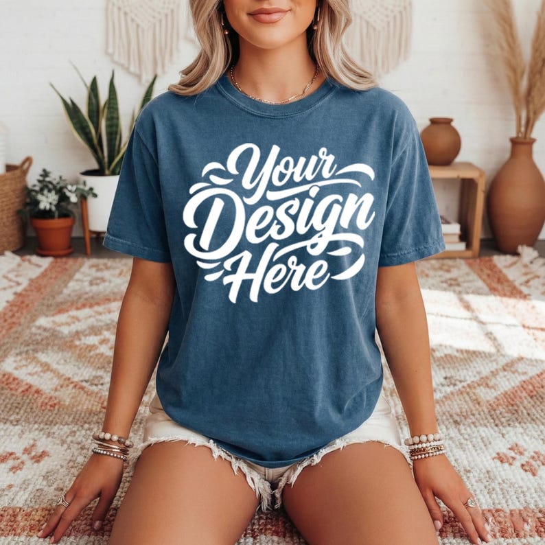 May include: A blue t-shirt with the text "Your Design Here" in white script. The shirt is a solid color and has a crew neck. The model is wearing white shorts and bracelets.