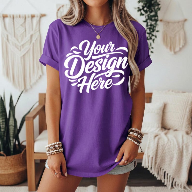 May include: A purple t-shirt with rolled-up sleeves. The shirt features the text "Your Design Here" in a white, cursive font. The model is wearing bracelets and a necklace.